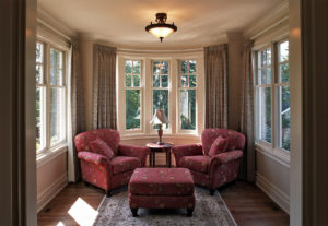 Two red arm chairs and matching ottoman in a small room with a bay window