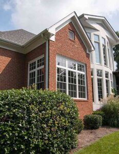 Brick home with large windows that is surrounded by shrubbery 